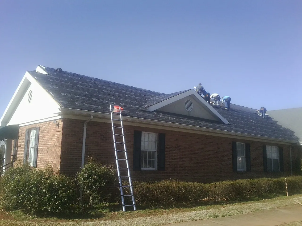 Crew tearing shingles off a brick ranch roof with a ladder set — Emergency Roof Repair work by our crew in Moultrie