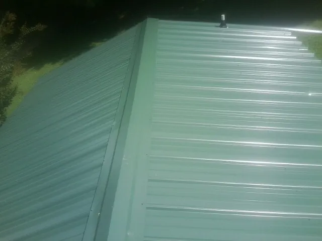 New green metal panels meeting at the ridge of a roof — Flat Roof Repair work by our crew in Moultrie