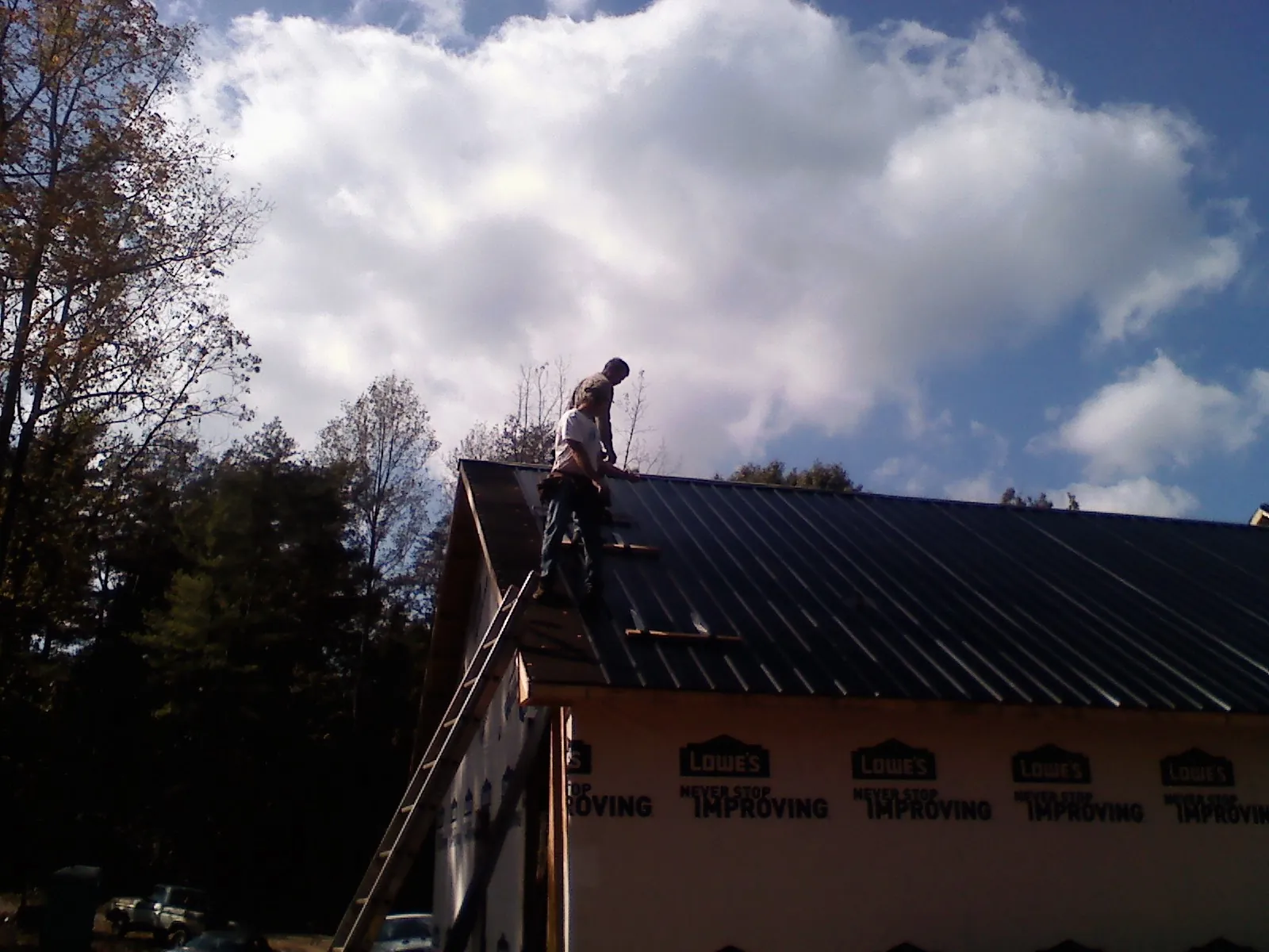 Roofer fastening dark metal panels high against a cloudy sky, from a Roof Inspection job in Moultrie