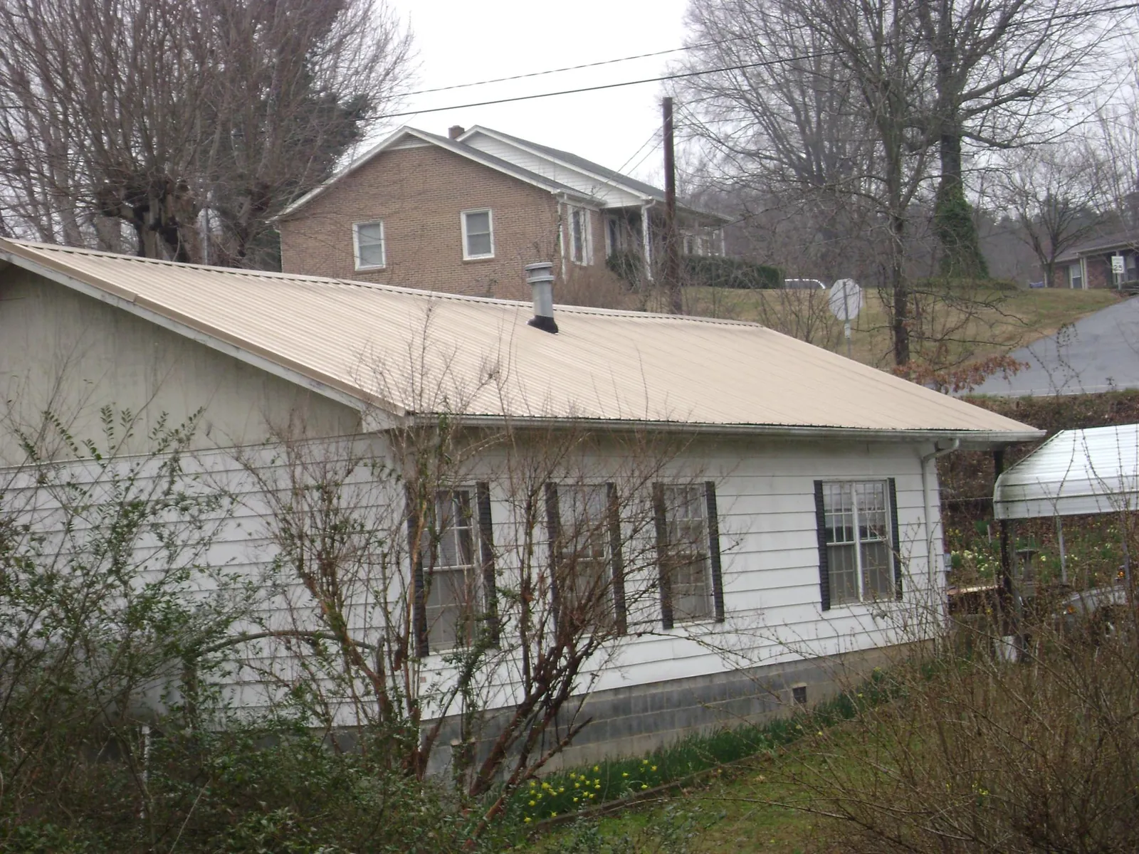 Tan metal roof on a white sided house set into a hillside — Commercial Roofing by Roofing Brothers in Moultrie